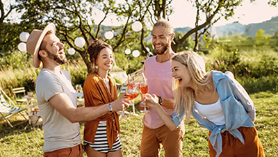 Vier junge Erwachsene stoßen lachend im Garten mit alkoholfreien Getränken an